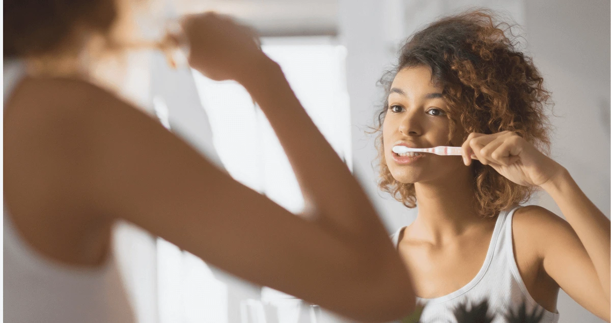 Vrouw met krulletjes kijkt in de spiegel en poetst haar tanden